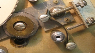 Note the two adjusting screws.The top one is a stop and the bottom the tension adjustment.  The plate that they are moving is a floating -- all directions idler gear that is thrust into the main gear and dial shaft quenching backlash.  The top gear in the photo below is attached to the tuning capacitor and is composed of two gears that are spring loaded to prevent back lash.